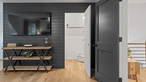 A modern room with a dark wooden wall, a wooden desk with a mirror, and a door leading to another room.