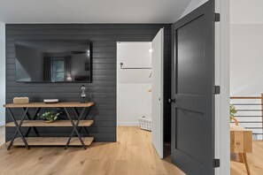Una habitación moderna con una pared de madera oscura, un escritorio de madera con un espejo y una puerta que conduce a otra habitación.
