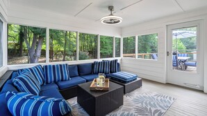 A covered outdoor seating area with a sectional sofa, a coffee table, and a view of the outdoors.