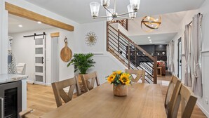 A modern kitchen with a built-in oven, a dining area with a wooden table and chairs, and a staircase leading to an upper level.