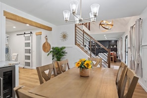 Una cocina moderna con horno empotrado, un comedor con mesa y sillas de madera, y una escalera que sube a un nivel superior.