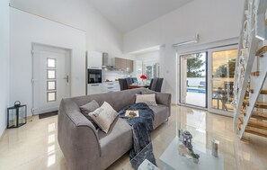 Ein modernes Wohnzimmer mit grauem Sofa, einem Glastisch und einem Essbereich mit Tisch und Stühlen.