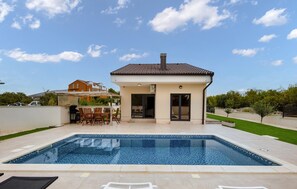 Ein modernes Haus mit Swimmingpool, Terrasse und überdachter Sitzgelegenheit im Freien.