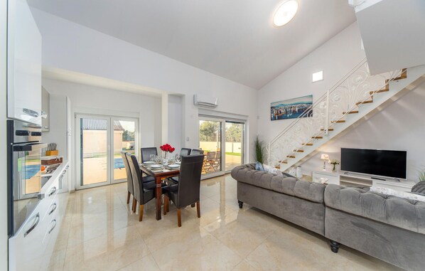 A modern living room with a sofa, a dining table with chairs, a TV, and a staircase. - Lovely home in Bilice (Bilice)