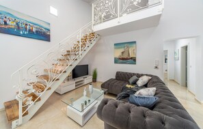 A modern living room with a staircase, a sofa, a TV, and artwork on the walls. - Lovely home in Bilice (Bilice)