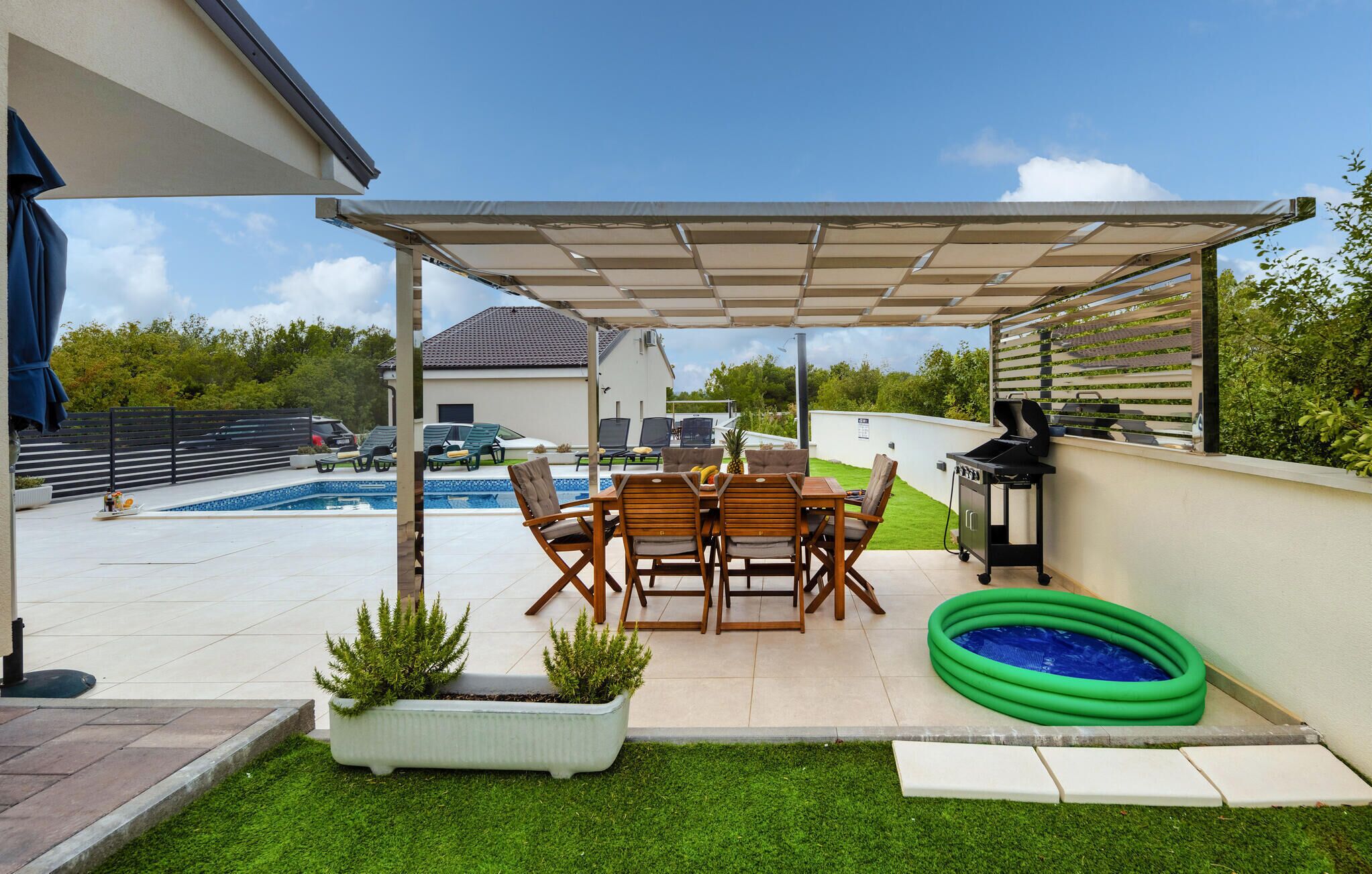 En overdækket terrasse med pool, grill og en lille oppustelig pool.