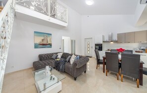 A modern living room with a grey sofa, a glass coffee table, and a dining area with a table and chairs. - Lovely home in Bilice (Bilice)