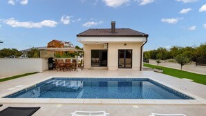 Una casa moderna con piscina, mobiliario de patio y cielo despejado.
