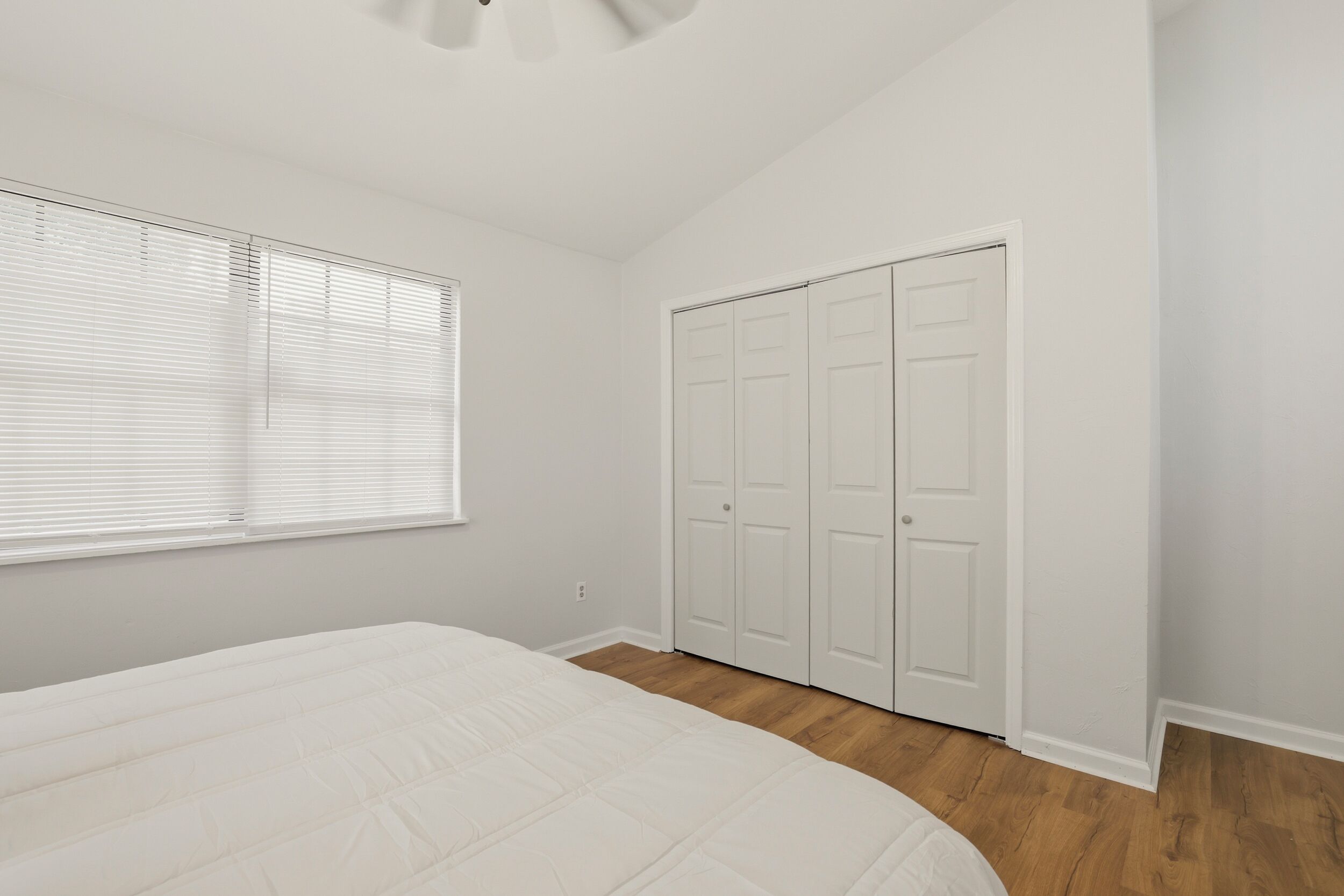Een slaapkamer met een bed, witte muren, een houten vloer en een kast met drie deuren.