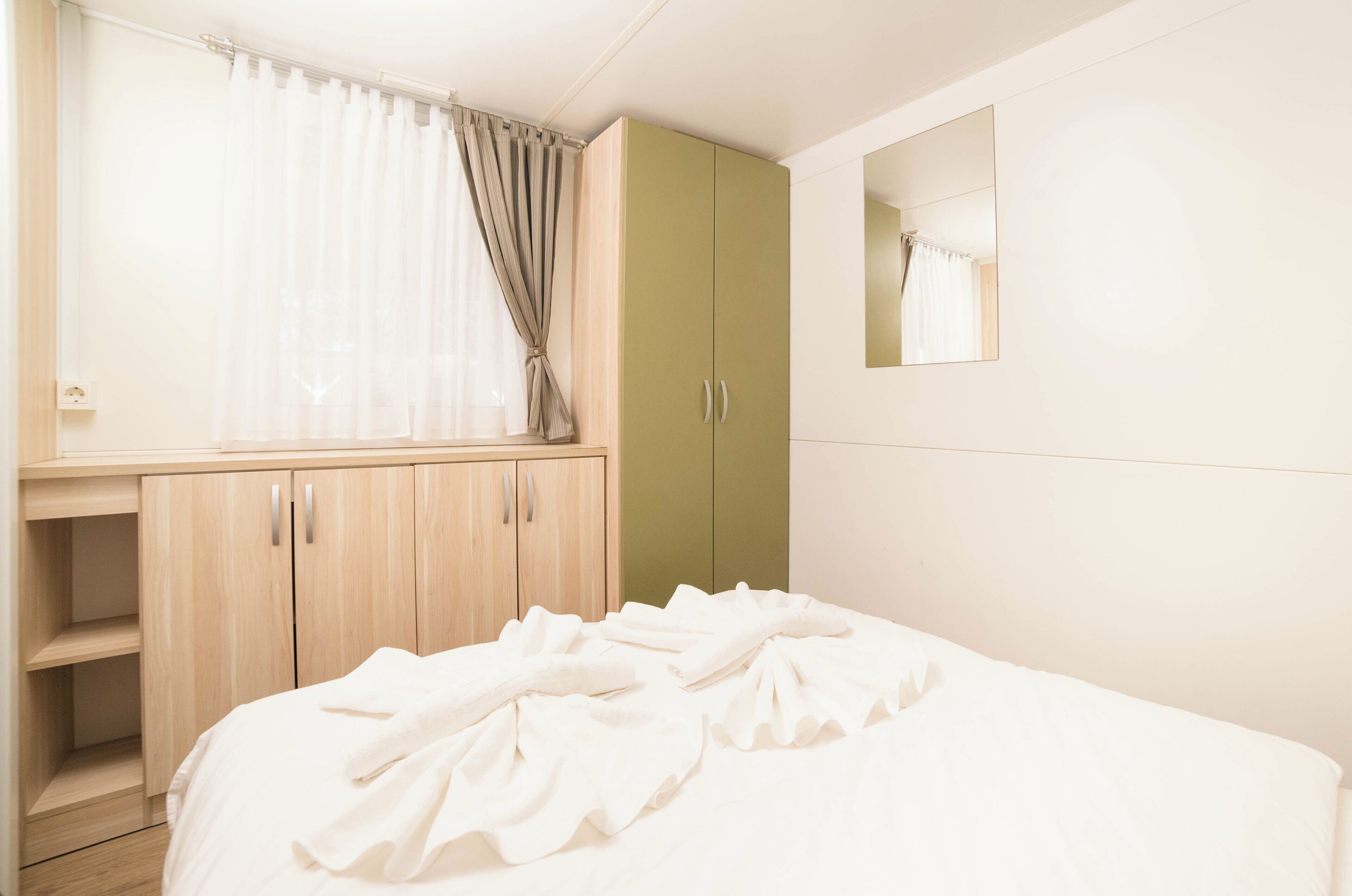 A bedroom with a bed, a wardrobe, a mirror, and a window with curtains.