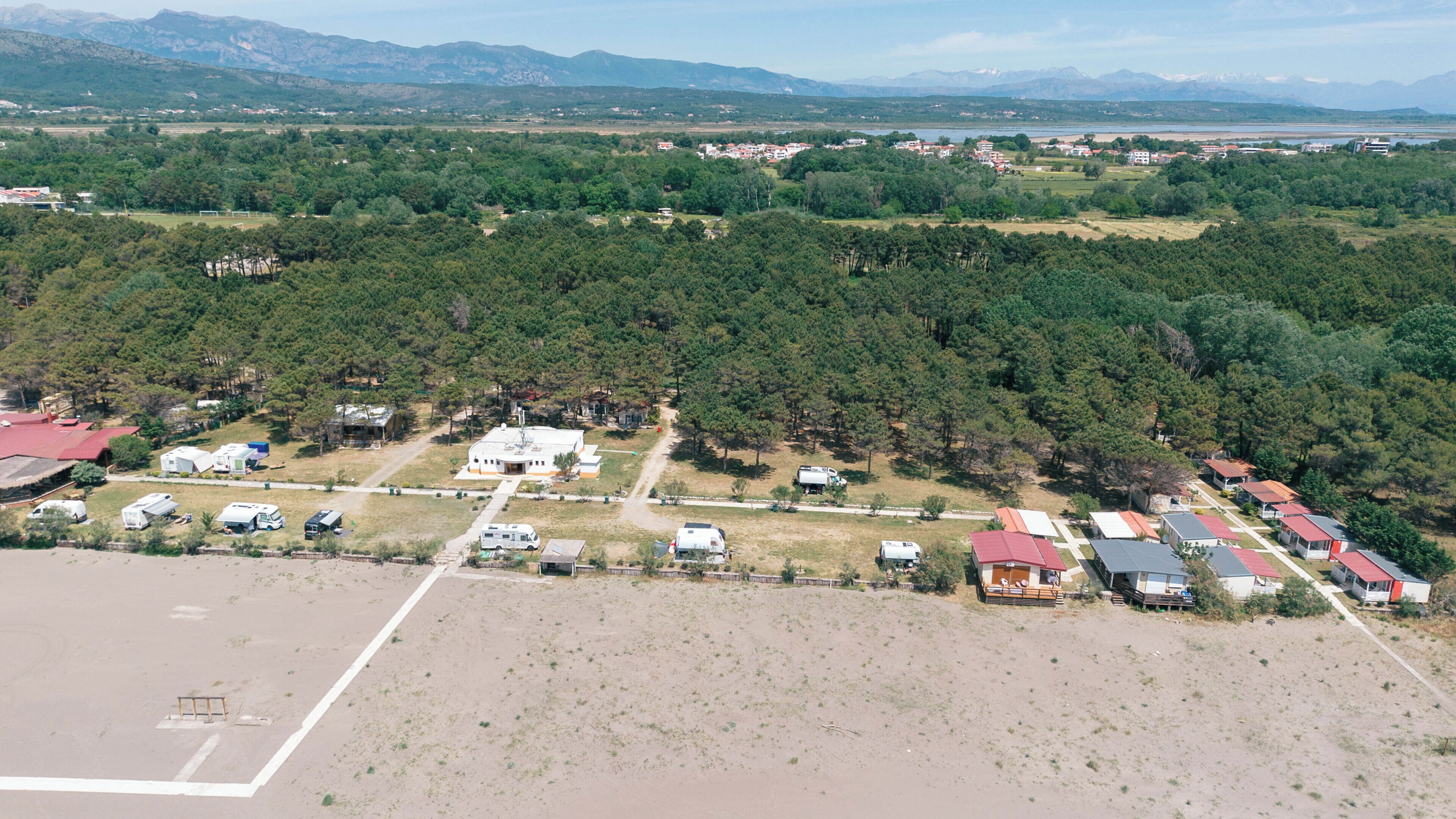 An aerial view of a campground with RVs, cabins, and a central building, surrounded by dense forest and mountains in the background.