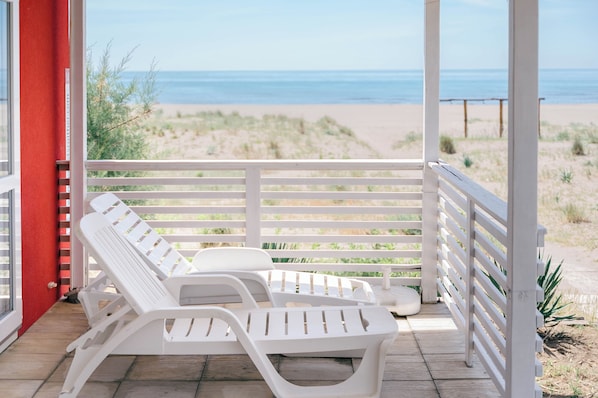 A covered outdoor area with white lounge chairs and a view of the beach. - Safari Beach & Camping (Ulcinj)