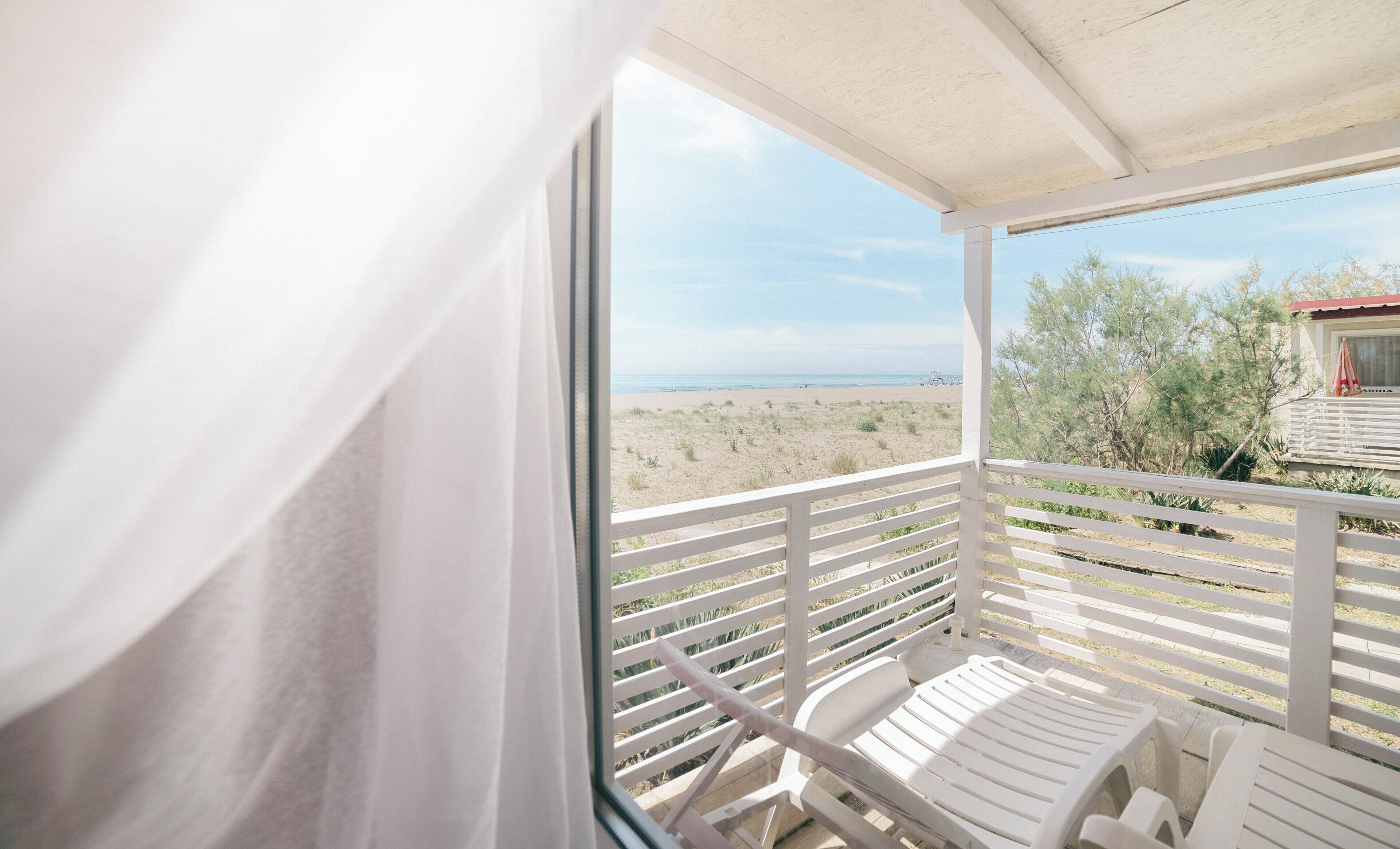 En balkon med hvide gelændere, en hvid stol og udsigt over stranden og havet.