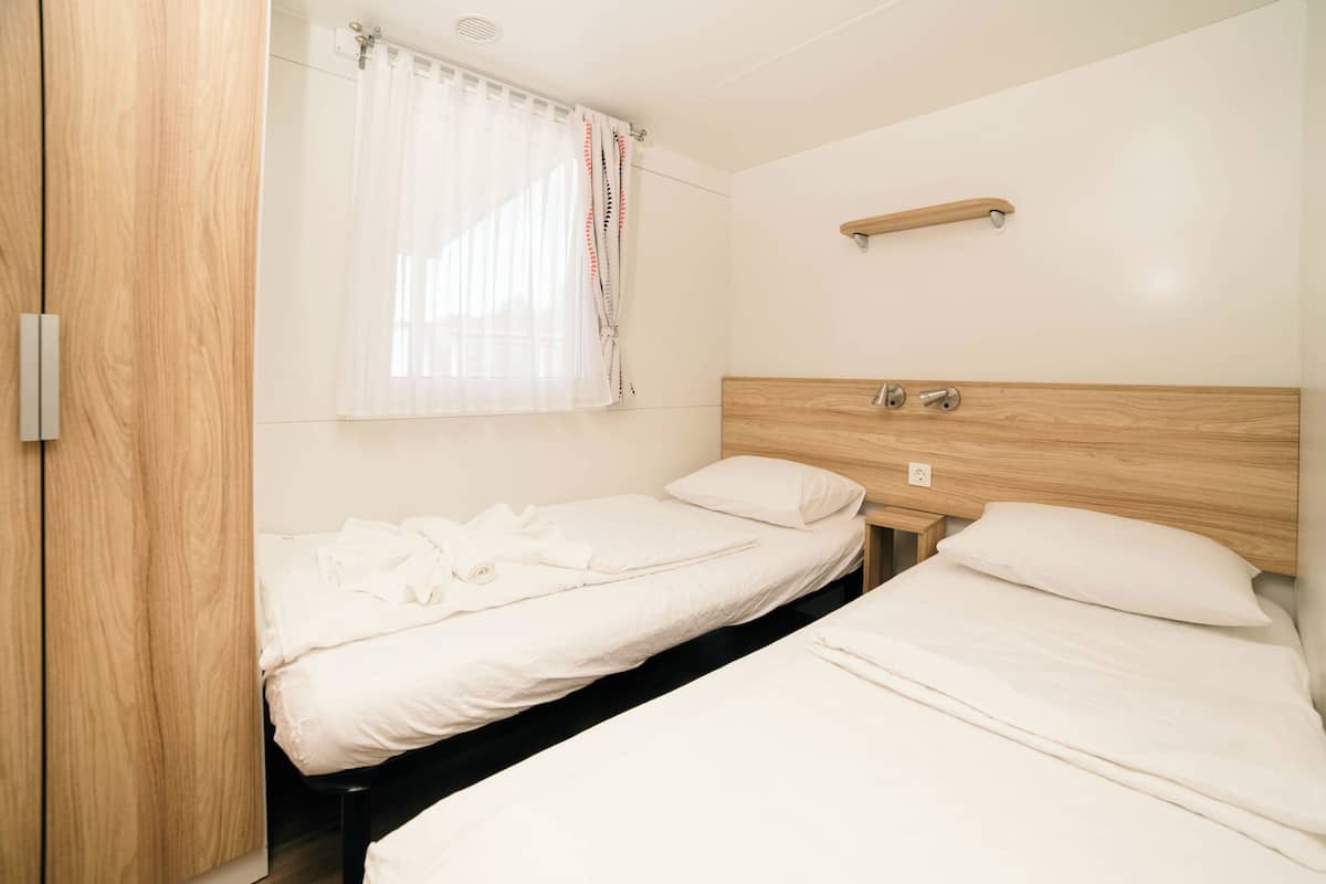 A bedroom with two beds, a wooden headboard, a bedside table, and a window with a curtain.