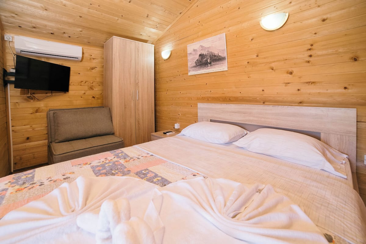 A wooden cabin-style room with a bed, a chair, an air conditioning unit, and a wall-mounted television.