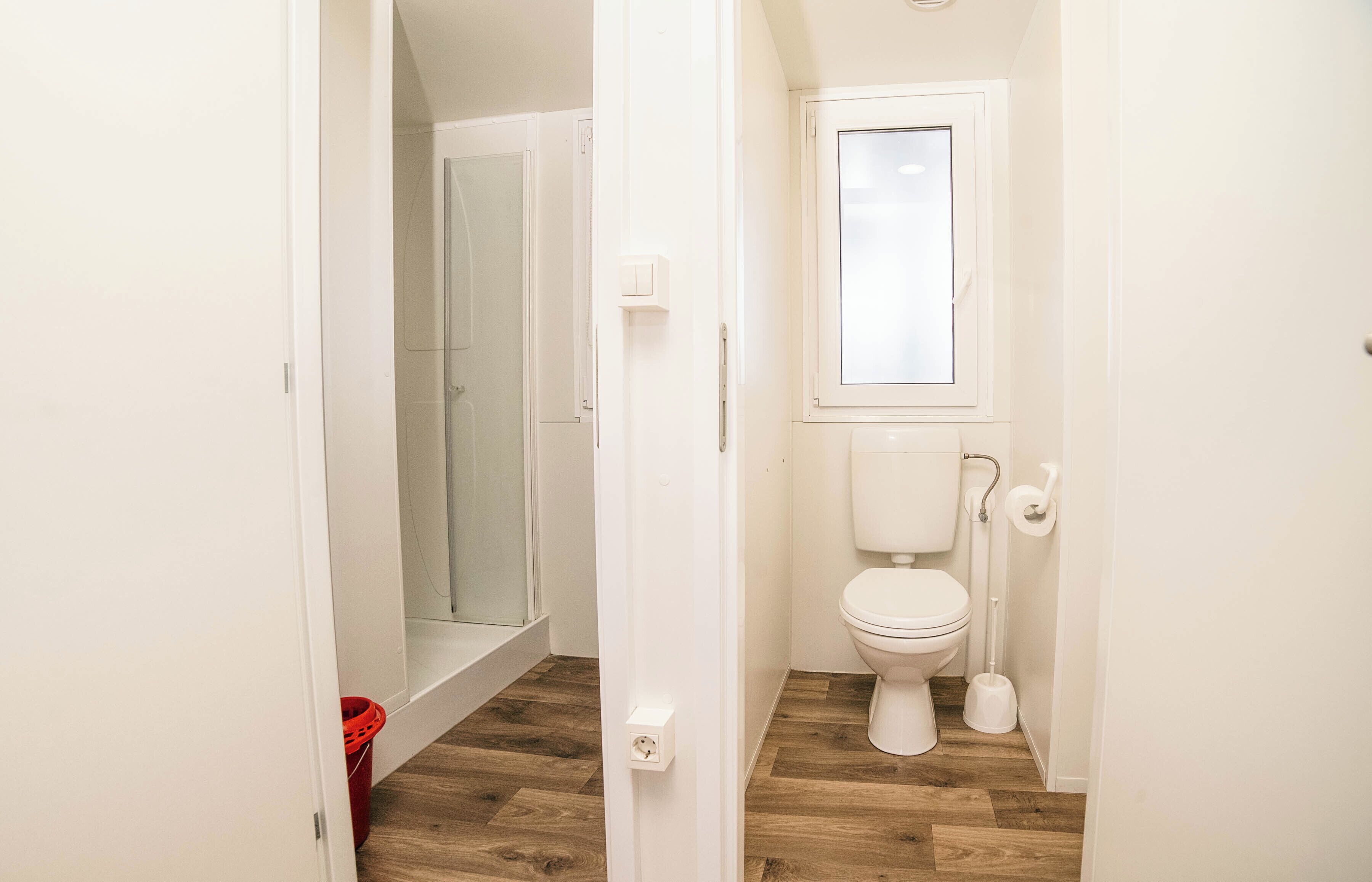 A narrow hallway leading to a bathroom with a toilet, bidet, and shower area.