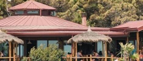 A building with a red roof and thatched roof structures, surrounded by greenery.