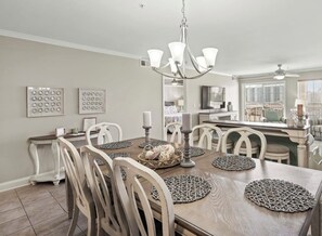 A dining area with a wooden table, white chairs, a chandelier, and wall art. - Welcome to Far Far Away at Ocean Marsh! (North Myrtle Beach)