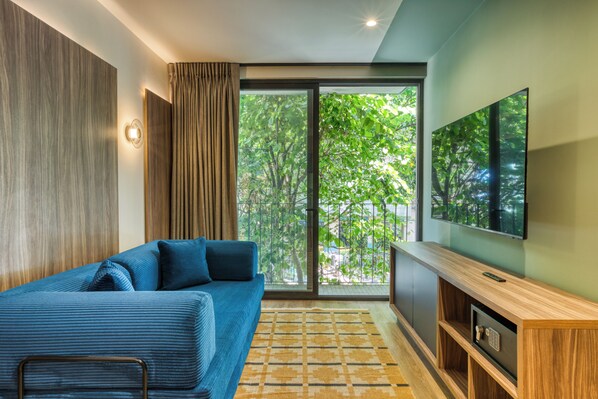 Un salon moderne avec un canapé, un téléviseur et une grande fenêtre donnant sur des arbres.
