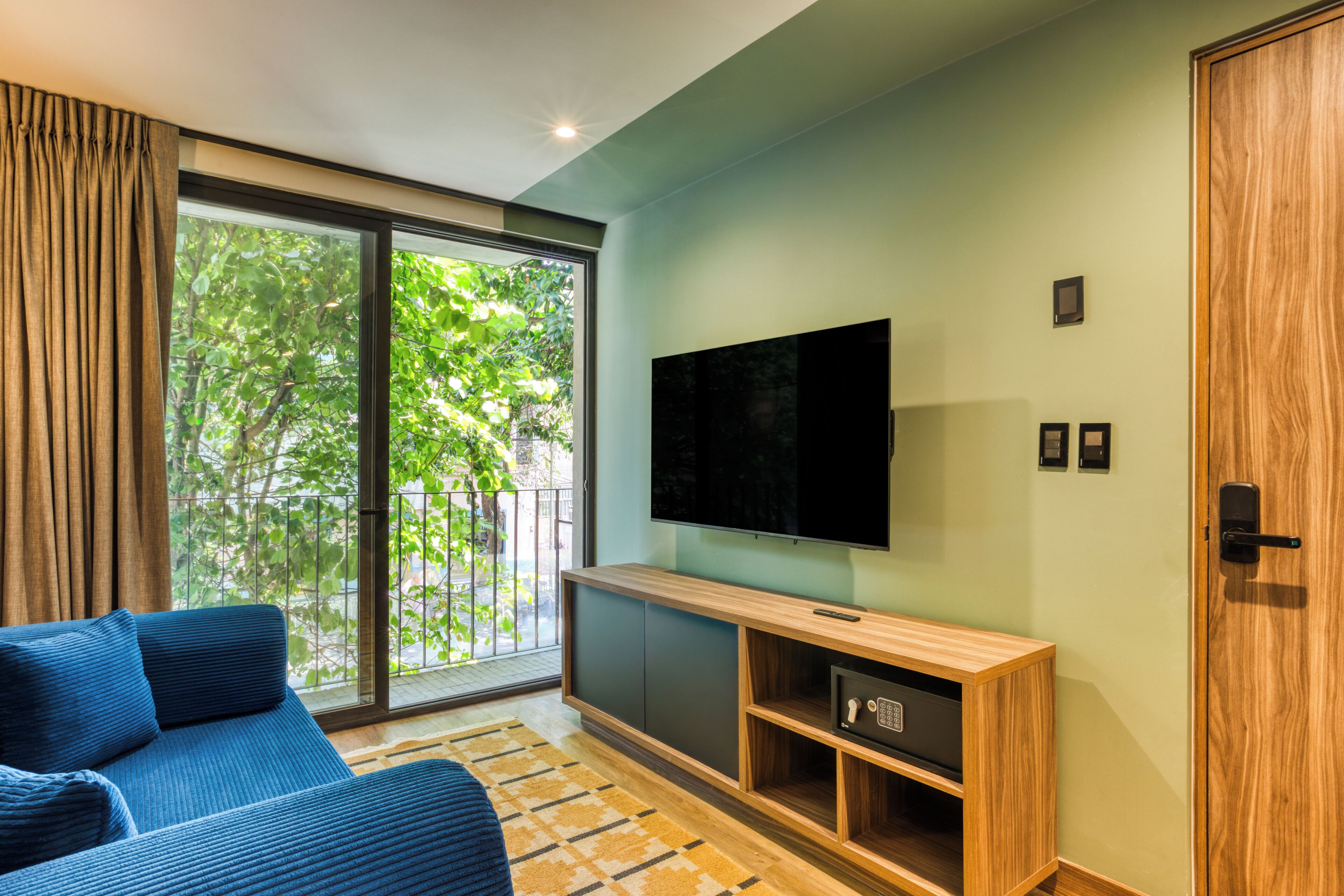 Un salon moderne avec un canapé, un téléviseur et une porte-fenêtre coulissante donnant sur un balcon.