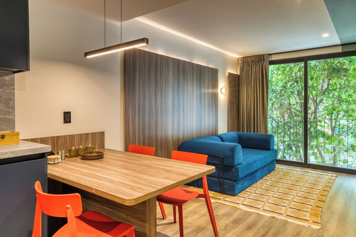A modern living room with a sofa, a dining table with chairs, and a large window with a view of trees.