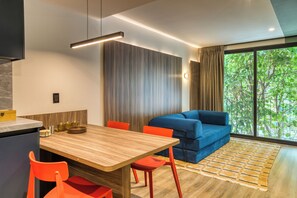 Un salon moderne avec un canapé, une table à manger et des chaises, ainsi qu’une grande fenêtre donnant sur la verdure.