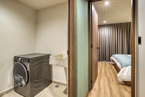 Une chambre d’hôtel compacte équipée d’une machine à laver, d’un petit lavabo et d’un lit muni d’un rideau.