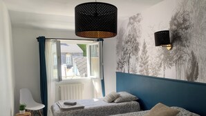 A bedroom with two beds, a chair, a radiator, and a window with curtains. - Triple Bright Room - Centre & Château (Lourdes)