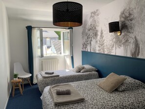 Een slaapkamer met twee bedden, een stoel, een radiator, een raam met gordijnen en een wandlamp.