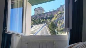 A room with a bed, a window with curtains, a radiator, and a view of a castle on a hill. - Triple Bright Room - Centre & Château (Lourdes)