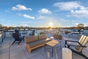 A rooftop terrace with outdoor seating, including a sofa and chairs, and a view of the sunset over a body of water. - Studio. East Nash. Mins to Broadway. Gym. Sky Deck (Nashville)