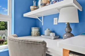 A room with a blue wall, a white desk, a grey chair, a white lamp, and a shelf with decorative items. - Studio. East Nash. Mins to Broadway. Gym. Sky Deck (Nashville)