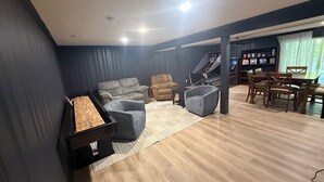 Un salon comprenant un canapé, des fauteuils, une table basse, une table à manger avec des chaises et un panier de basket.