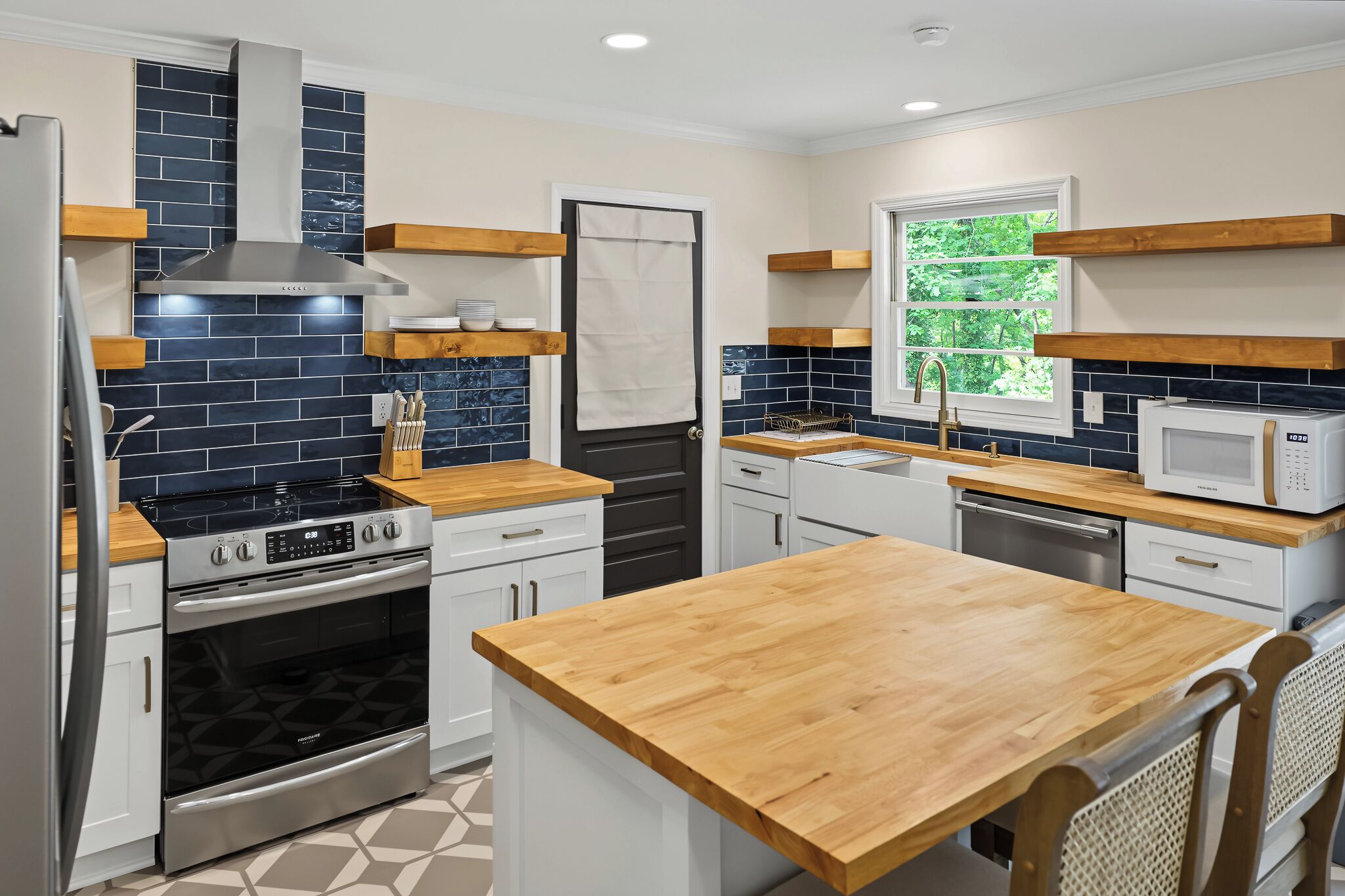 A modern kitchen with a central island, built-in oven, microwave, and a window providing a view of greenery.