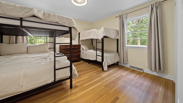Une pièce avec des lits superposés, une commode en bois, une fenêtre avec des rideaux et un luminaire au plafond.
