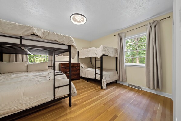 Una habitación con literas, un aparador de madera, una ventana con cortinas y una lámpara en el techo.