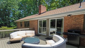 Une terrasse extérieure avec un canapé en osier, une table basse en verre et un barbecue.