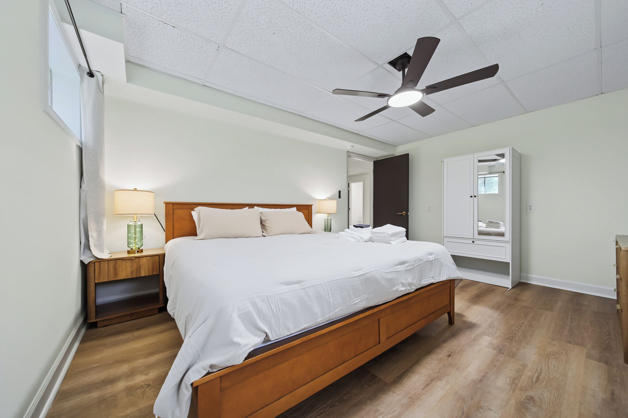 A bedroom with a wooden bed, a ceiling fan, a nightstand with a lamp, and a wardrobe.