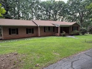 A two-story brick house with a front porch, a well-maintained lawn, and a driveway. - Lakefront 5BR Retreat w/ Private Dock  —Boat Ramp Across Street — Sleeps 14+ (Clarksville)