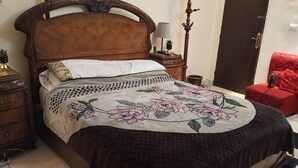 Ein Schlafzimmer mit einem hölzernen Bett, einem roten Sessel, einem Nachttisch, einer Lampe und einem an der Wand befestigten Regal.