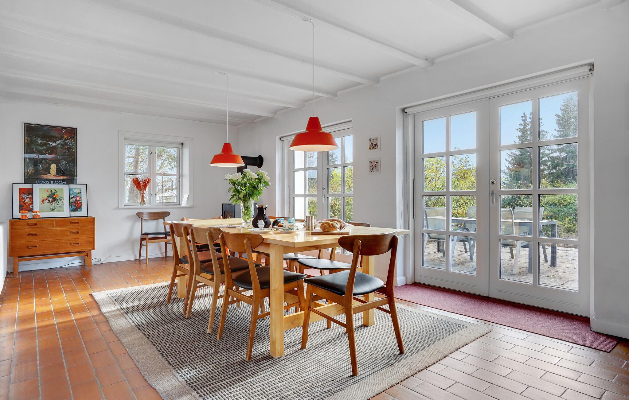 A dining area with a wooden table, chairs, a rug, and a red pendant light.