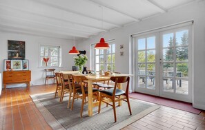 A dining area with a wooden table, chairs, a rug, and a red pendant light. - Cozy home in Glesborg with house sea view (Glesborg)