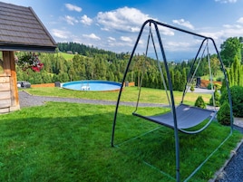 A backyard with a swing set, a swimming pool, and a wooden cabin.
