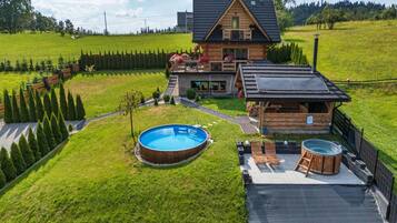 A wooden house with a swimming pool, a hot tub, and a fenced yard.