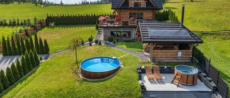 A wooden house with a swimming pool, a hot tub, and a fenced yard.