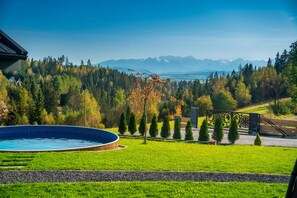 Una piscina rodeada de un césped cuidado, con vistas a un bosque y montañas al fondo.