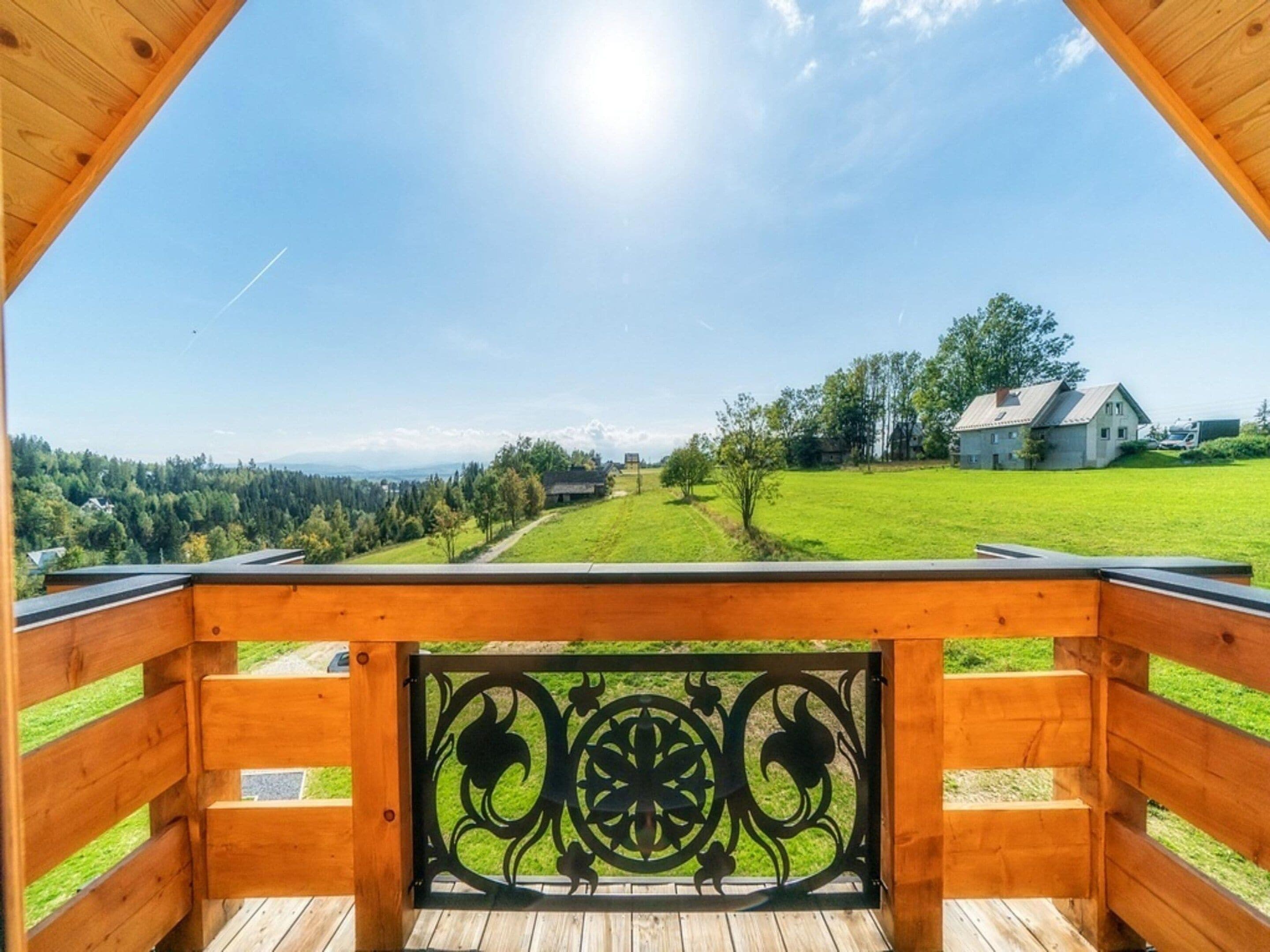 Um deck de madeira com guarda-corpo de metal, com vista para uma paisagem verde com árvores e uma casa.