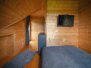 A cabin room with a sloped ceiling, a bed, a small cabinet, and a television mounted on the wall. - Luxury Holiday Villa, Pool, Sauna, Jacuzzi (Nowy Targ)