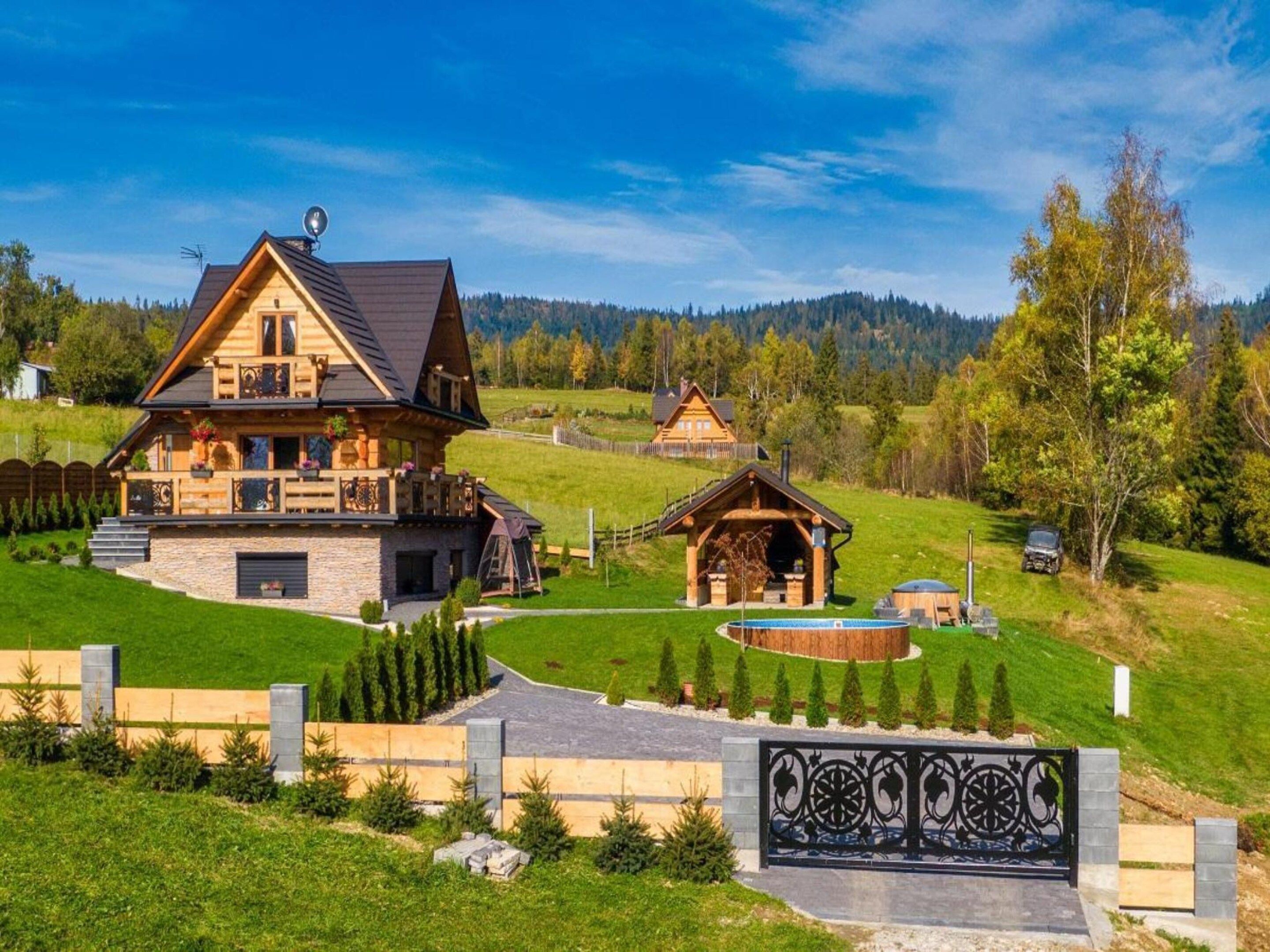 A large wooden house with a stone foundation, a covered outdoor area, and a well-maintained lawn.