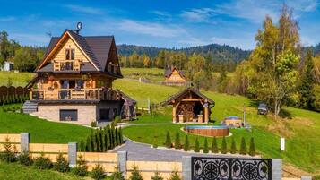 A large wooden house with a stone foundation, a covered outdoor area, and a well-maintained lawn.